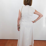 Woman wearing a white dress standing against a white wall.