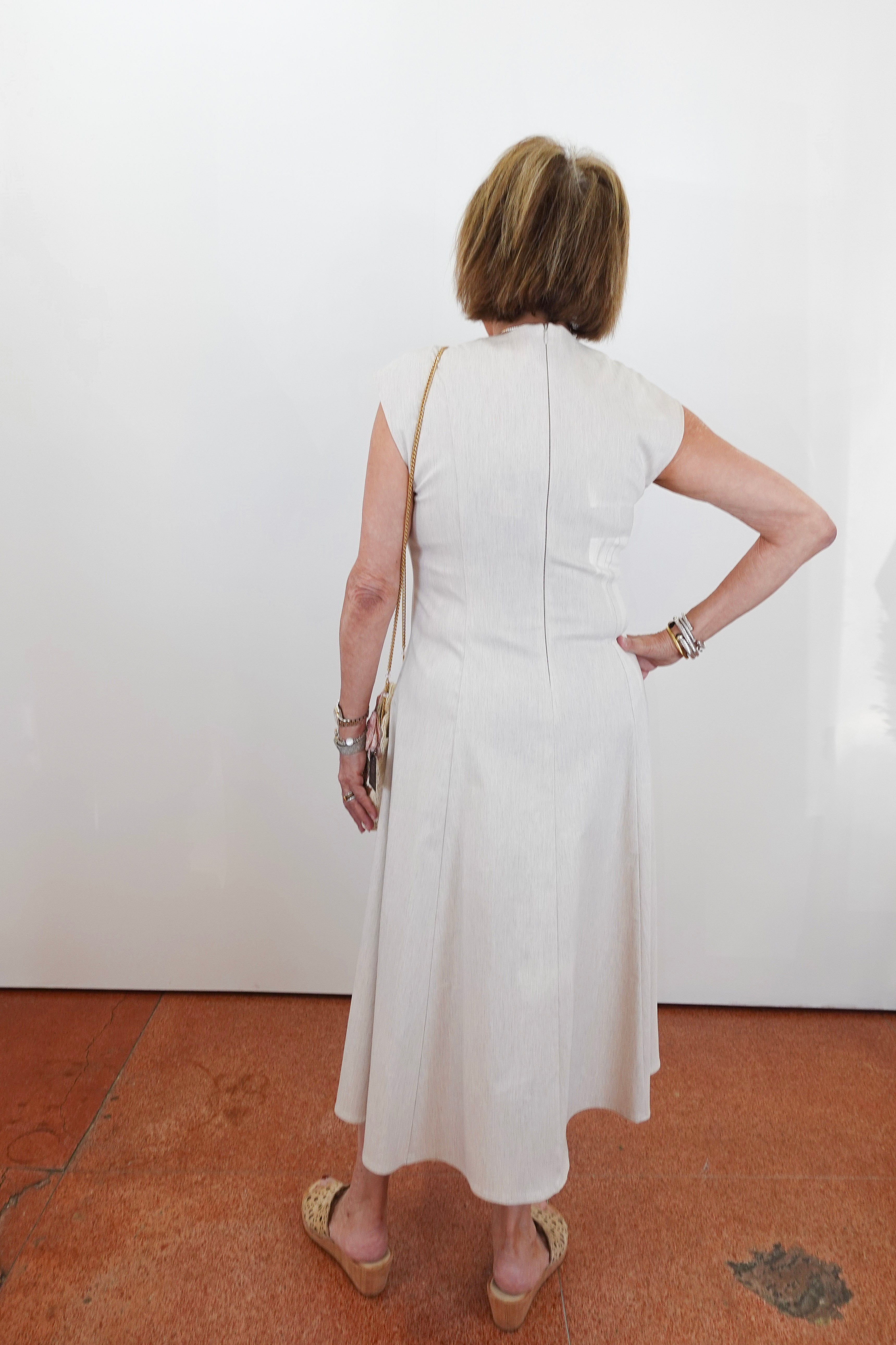 Woman wearing a white dress standing against a white wall.