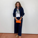 Woman in navy outfit with orange clutch against a white wall