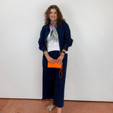 Woman in navy outfit with orange clutch against a white wall