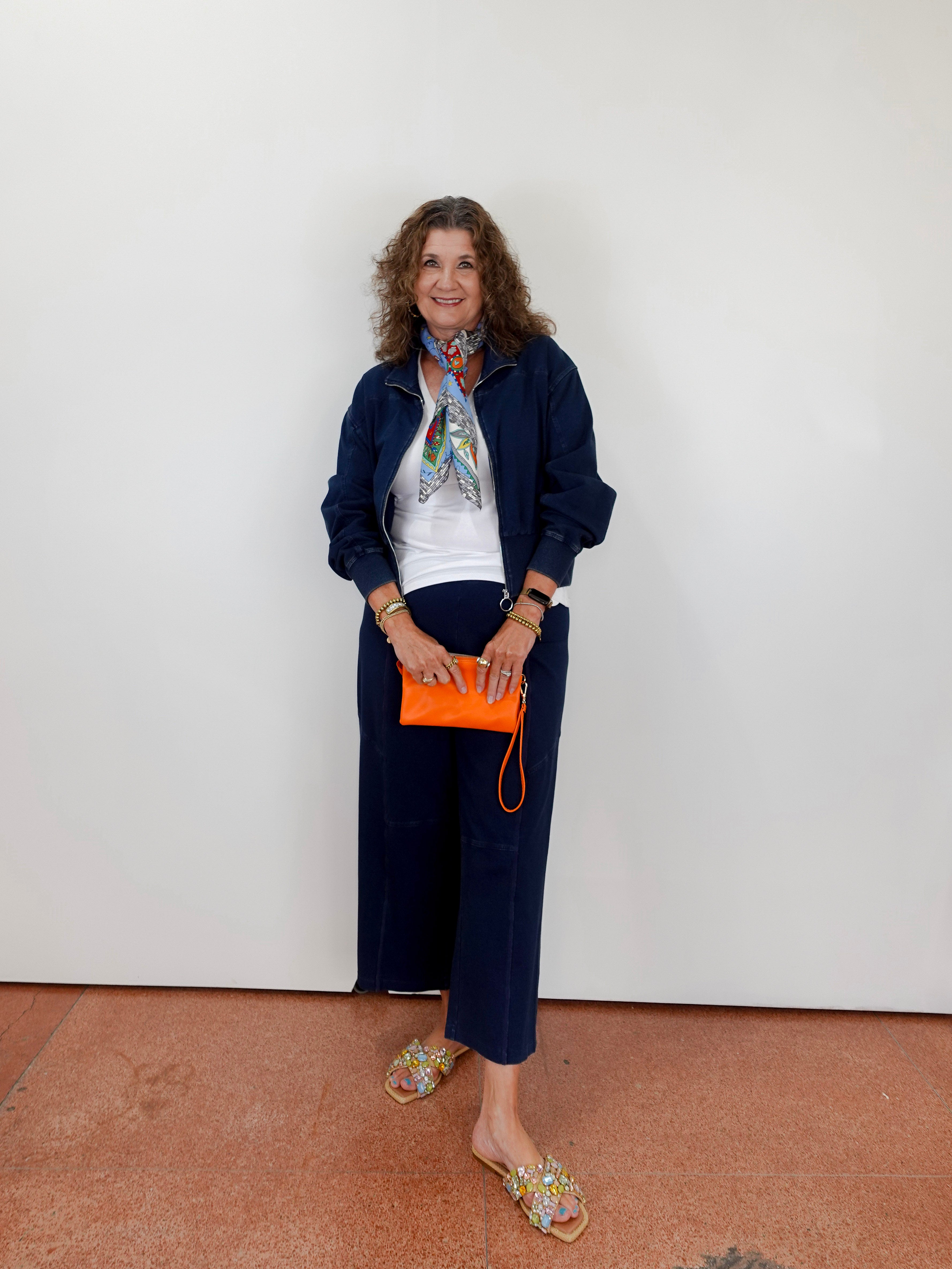 Woman in navy outfit with orange clutch against a white wall
