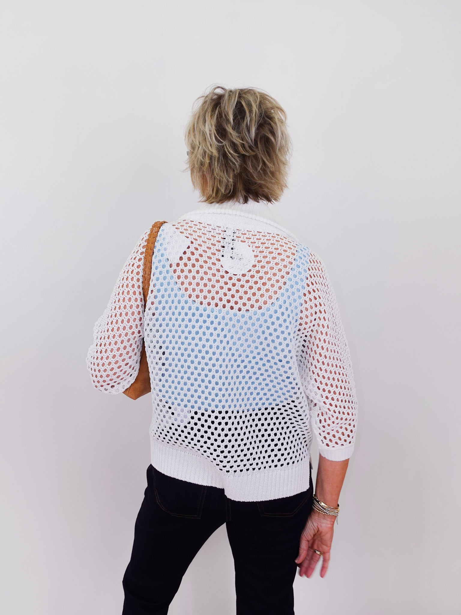 Person wearing a white mesh top with a plain background