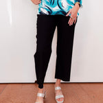 Person wearing a colorful top and black pants with white sandals on a plain background