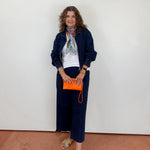 Woman in navy outfit with orange clutch against a white wall