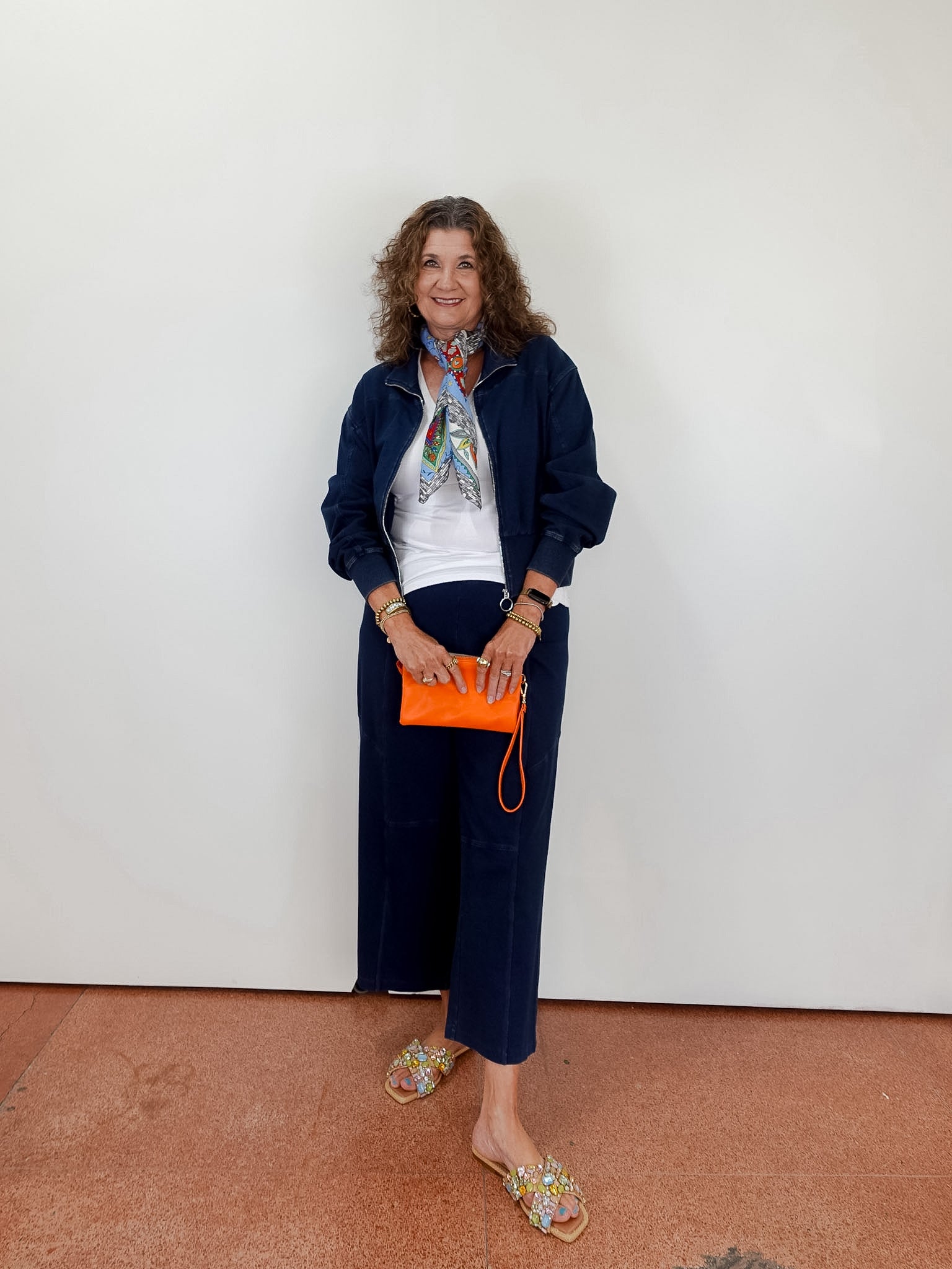 Woman in navy outfit with orange clutch against a white wall