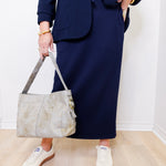 Person wearing a navy blue suit holding a beige handbag indoors.