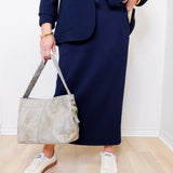 Person wearing a navy blue suit holding a beige handbag indoors.