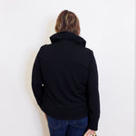Person wearing a black jacket and blue jeans against a white background