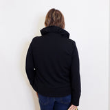 Person wearing a black jacket and blue jeans against a white background