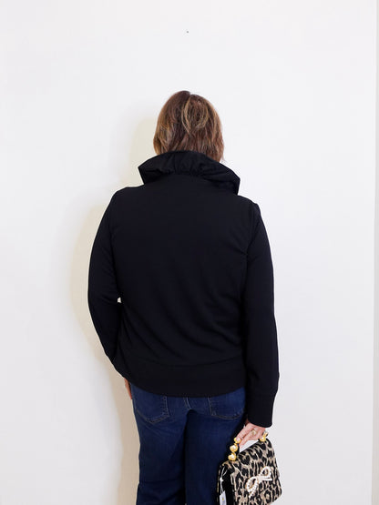 Person wearing a black jacket and blue jeans against a white background