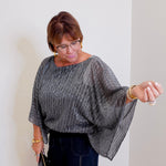 Women wearing a Joseph ribkoff sequin pleated knit top that is black and silver against a white wall. 