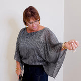 Women wearing a Joseph ribkoff sequin pleated knit top that is black and silver against a white wall. 