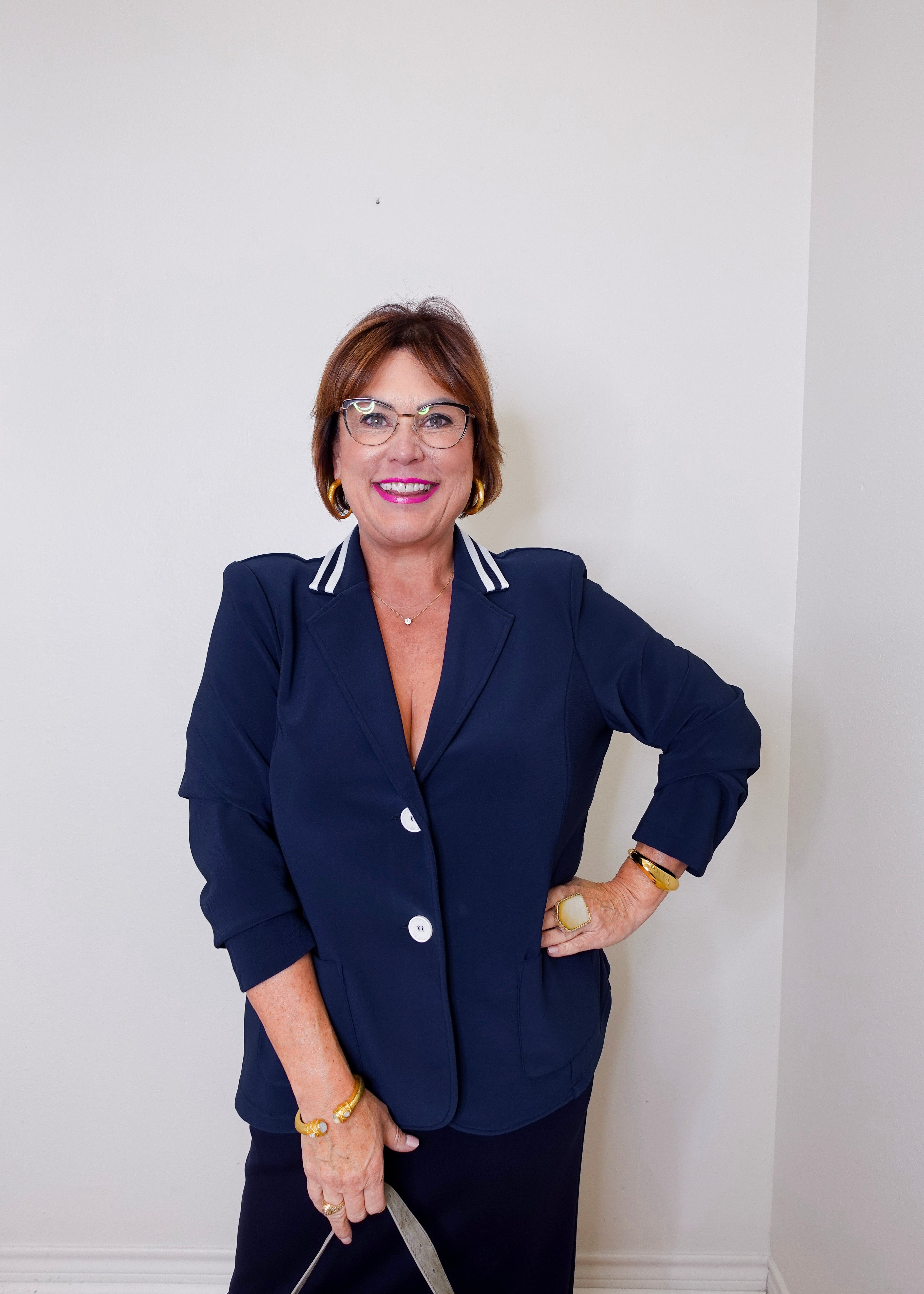 Woman wearing a navy blazer with white trim against a plain background