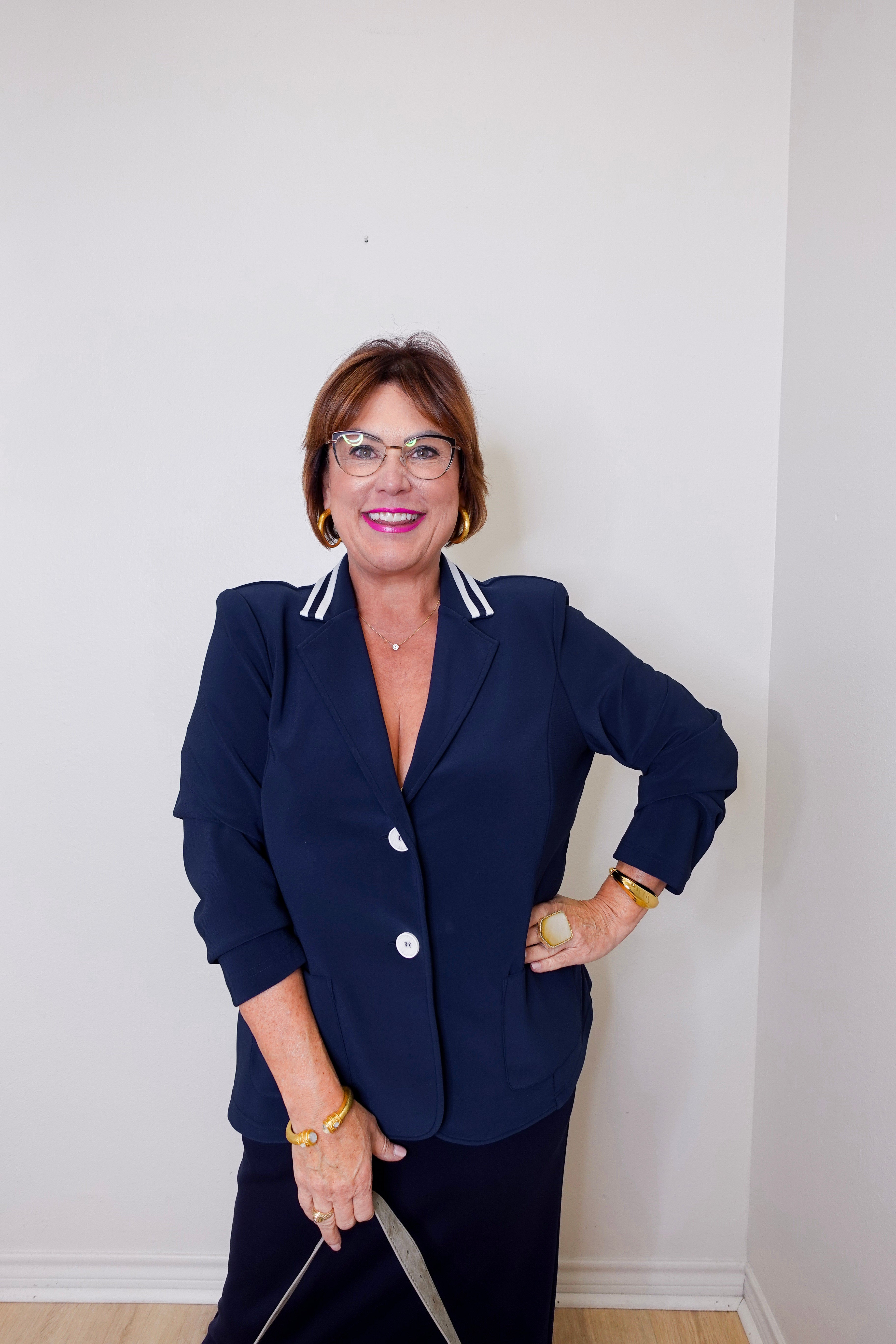 Woman wearing a navy blazer with white trim against a plain background