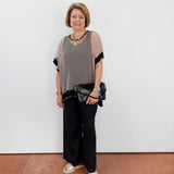Woman wearing a patterned top and black pants against a white wall.