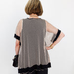 Woman wearing a patterned blouse with sheer sleeves against a white wall.