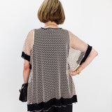 Woman wearing a patterned blouse with sheer sleeves against a white wall.