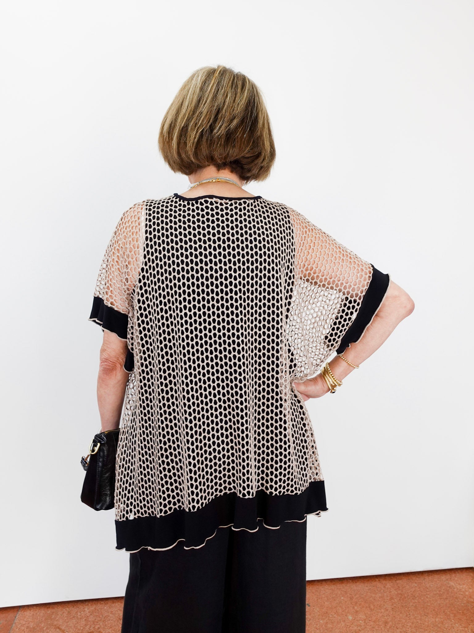Woman wearing a patterned blouse with sheer sleeves against a white wall.