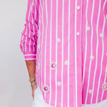 Person wearing a pink and white striped shirt with decorative buttons on a plain background