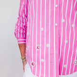 Person wearing a pink and white striped shirt with decorative buttons on a plain background