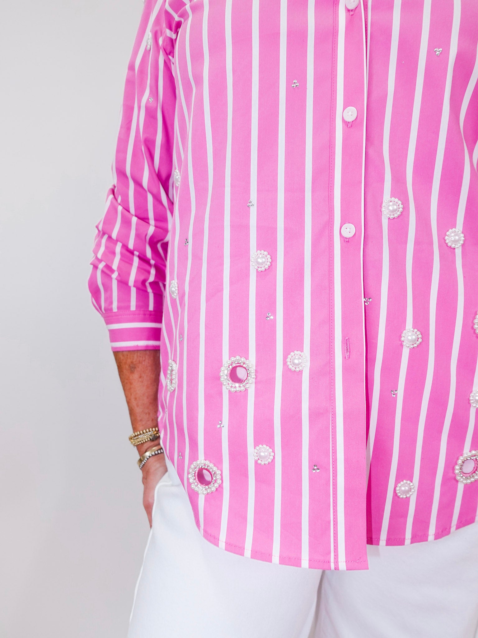 Person wearing a pink and white striped shirt with decorative buttons on a plain background
