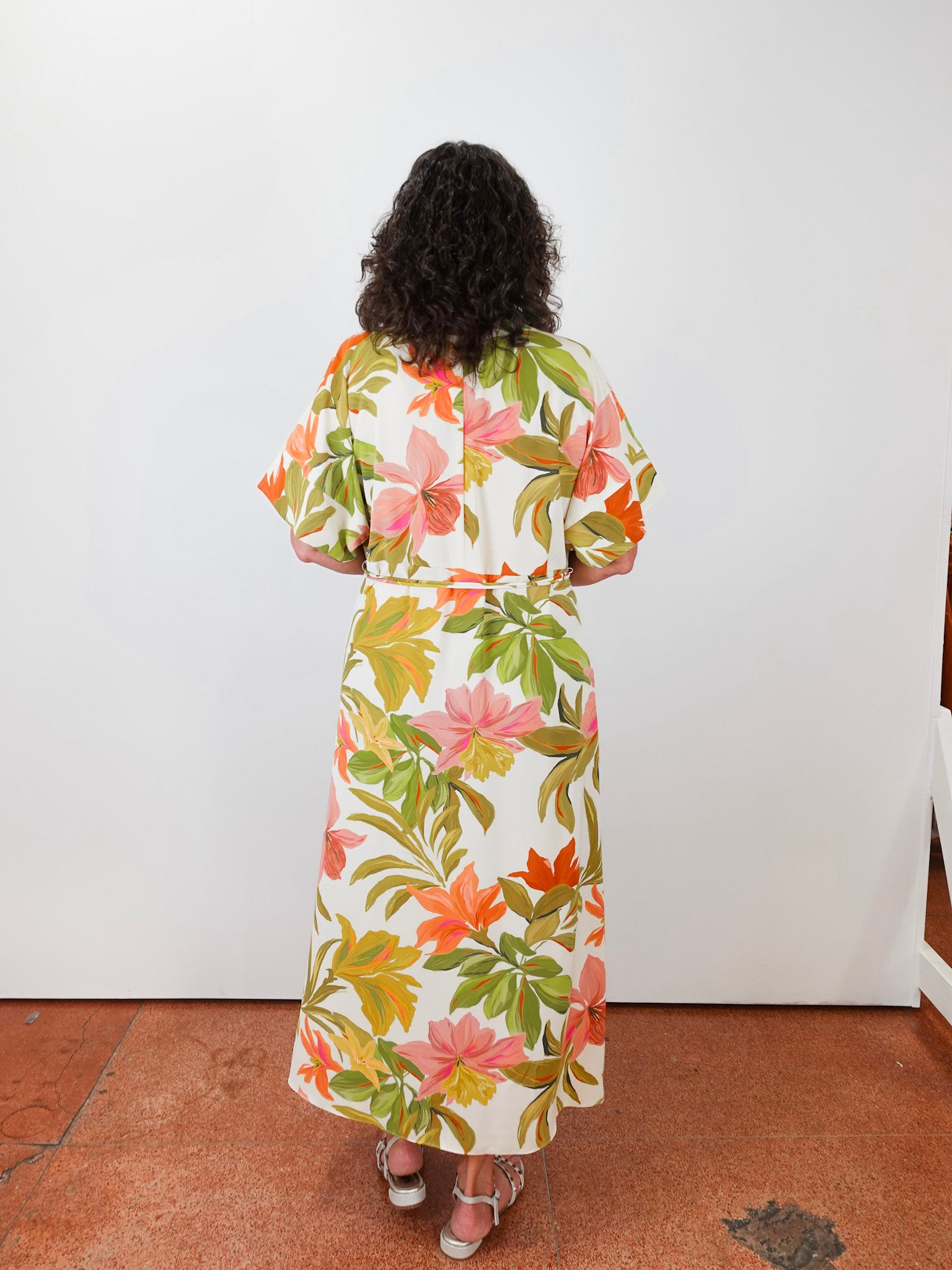 Person wearing a floral dress standing against a white wall.