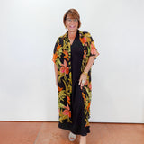 Woman wearing a black dress with a colorful floral kimono-style cover-up against a white wall.