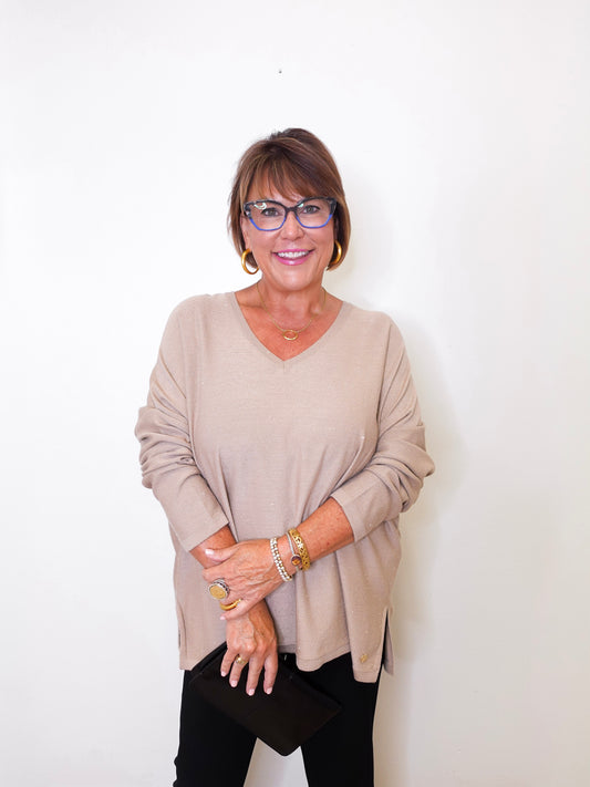 A women wearing a v-neck jewel embellished sweater in front of a white wall.