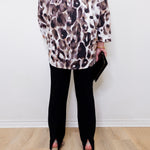 Person wearing a leopard print top and black pants against a white wall.