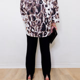 Person wearing a leopard print top and black pants against a white wall.