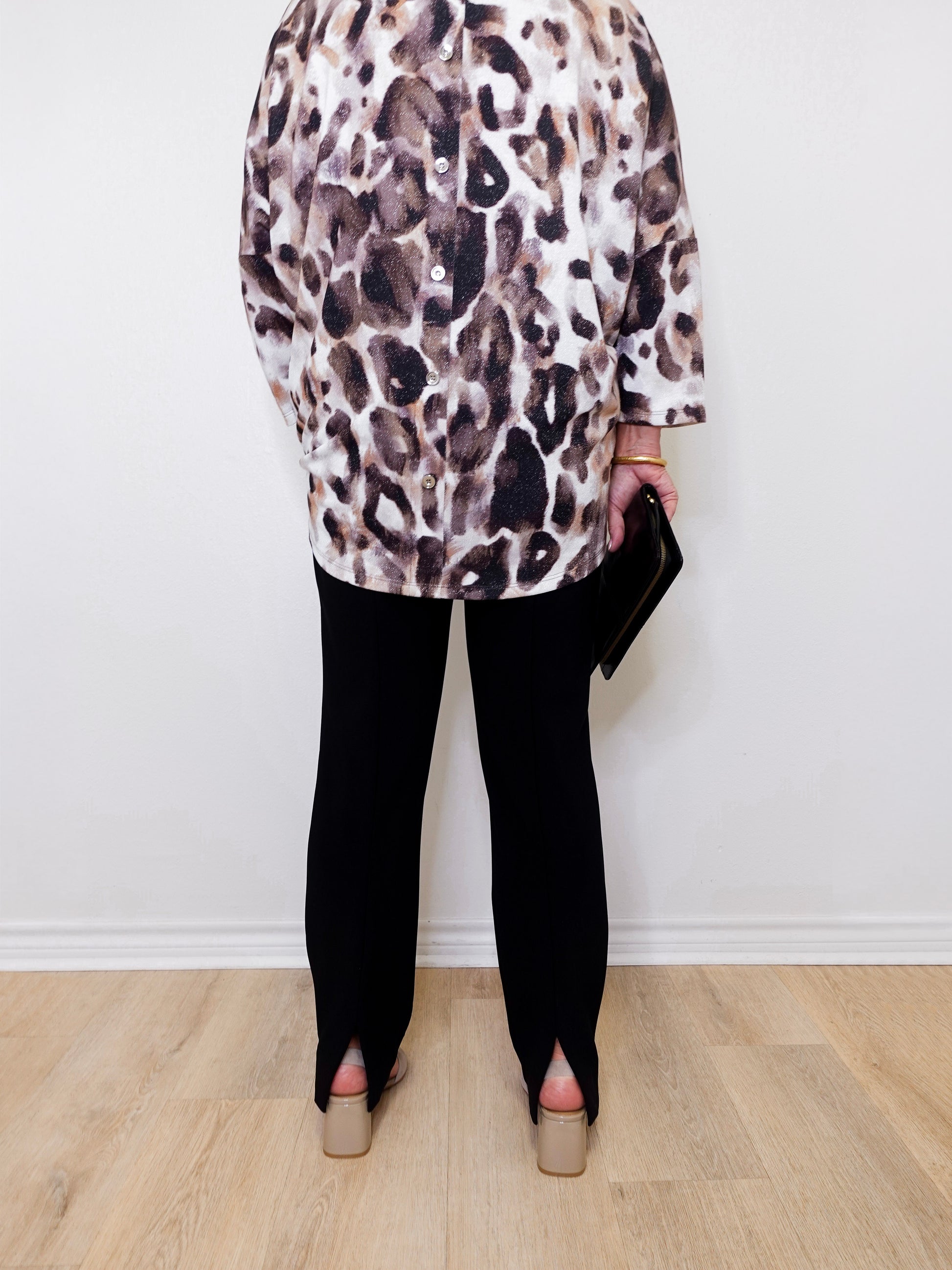 Person wearing a leopard print top and black pants against a white wall.