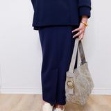 Person wearing a navy outfit with a beige handbag against a white wall.