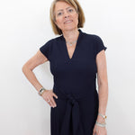 Woman wearing a navy blue dress holding a blue handbag against a white background
