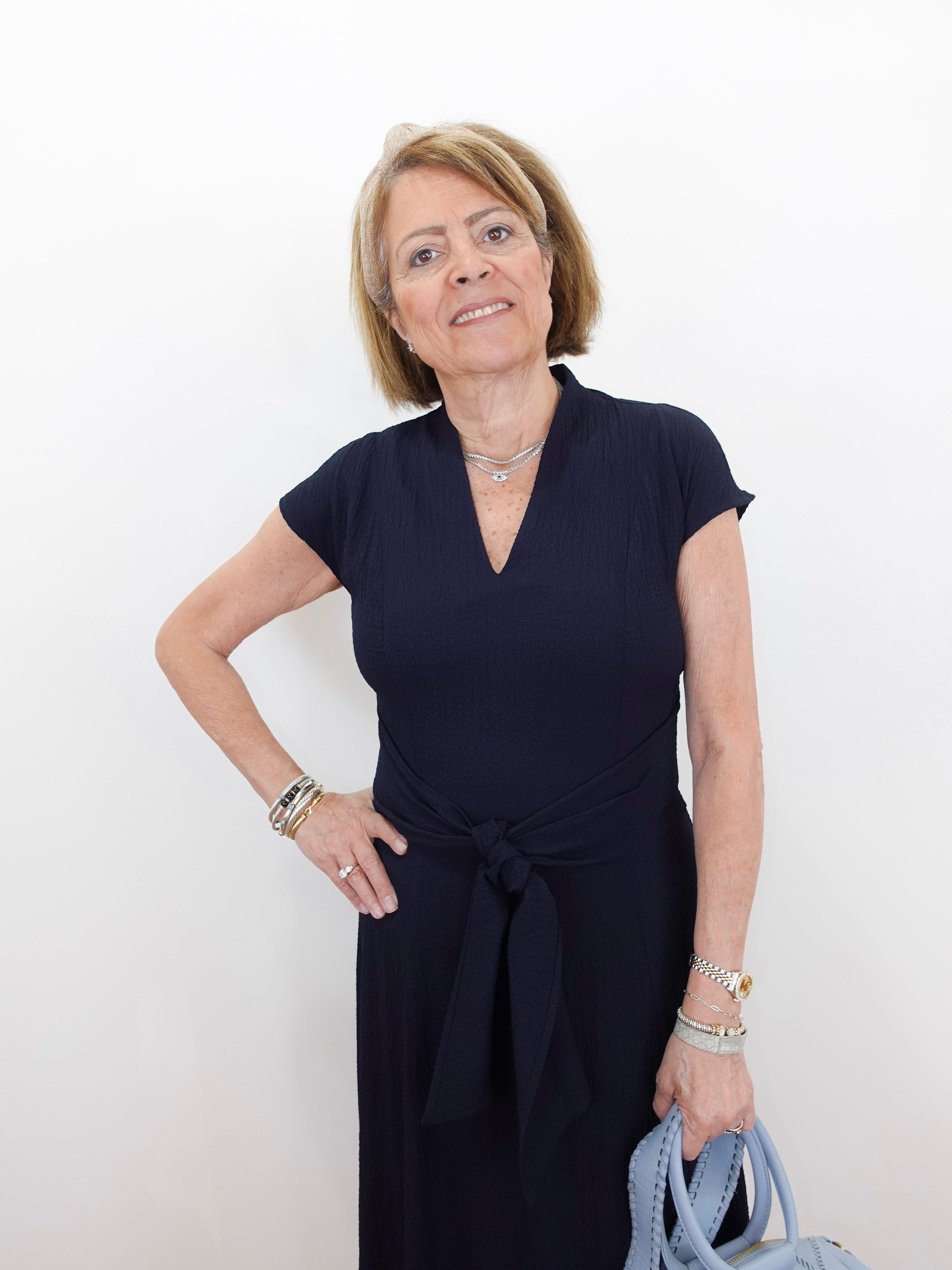 Woman wearing a navy blue dress holding a blue handbag against a white background