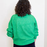Person wearing a green sweater against a white wall
