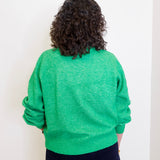 Person wearing a green sweater against a white wall