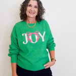 Woman wearing a green sweater with 'JOY' and a pink bow design.