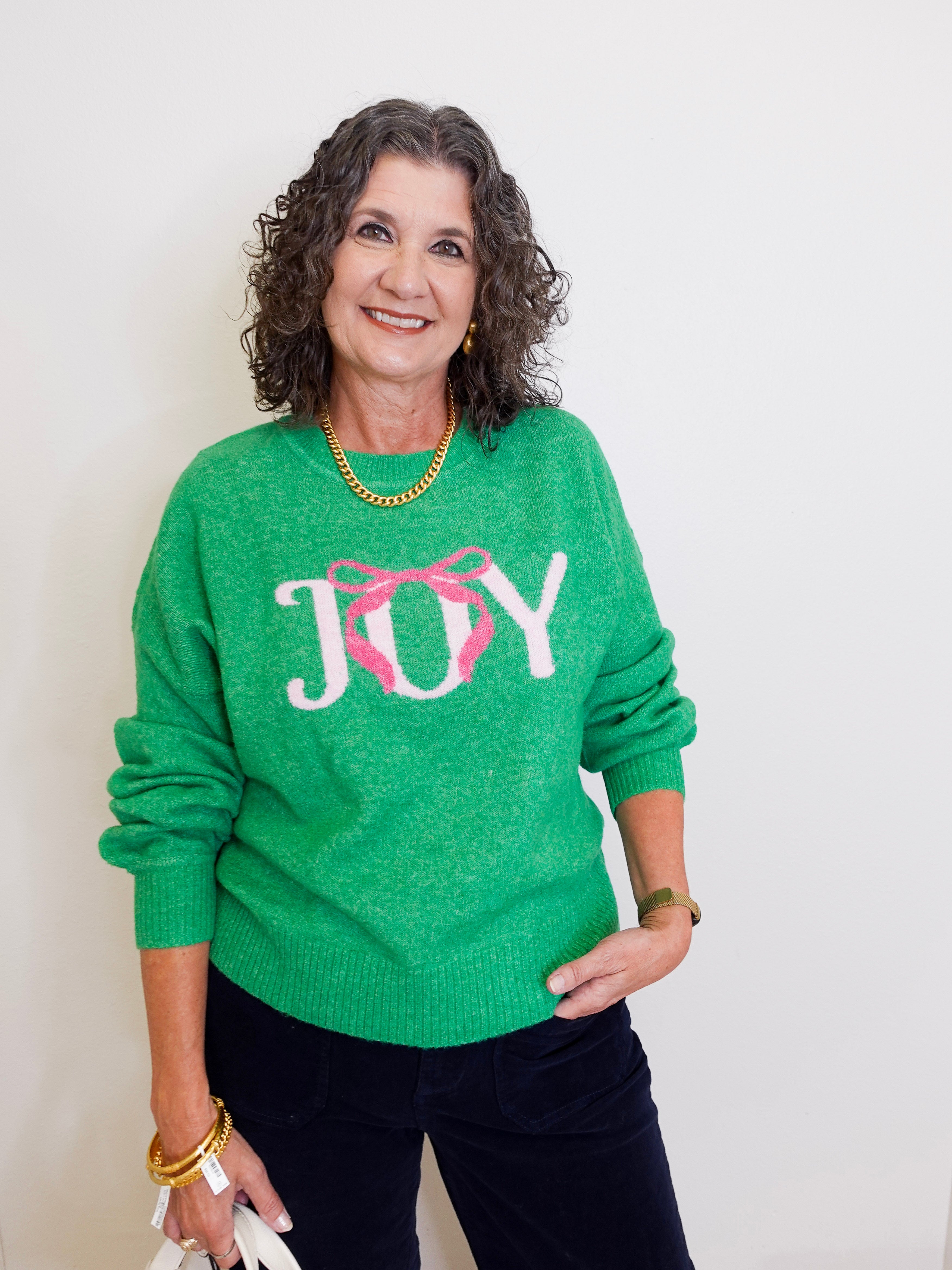 Woman wearing a green sweater with 'JOY' and a pink bow design.