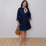 Woman wearing a denim dress with a white wall background