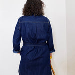 Person wearing a blue denim dress against a white wall