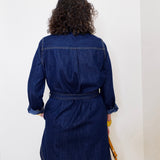 Person wearing a blue denim dress against a white wall