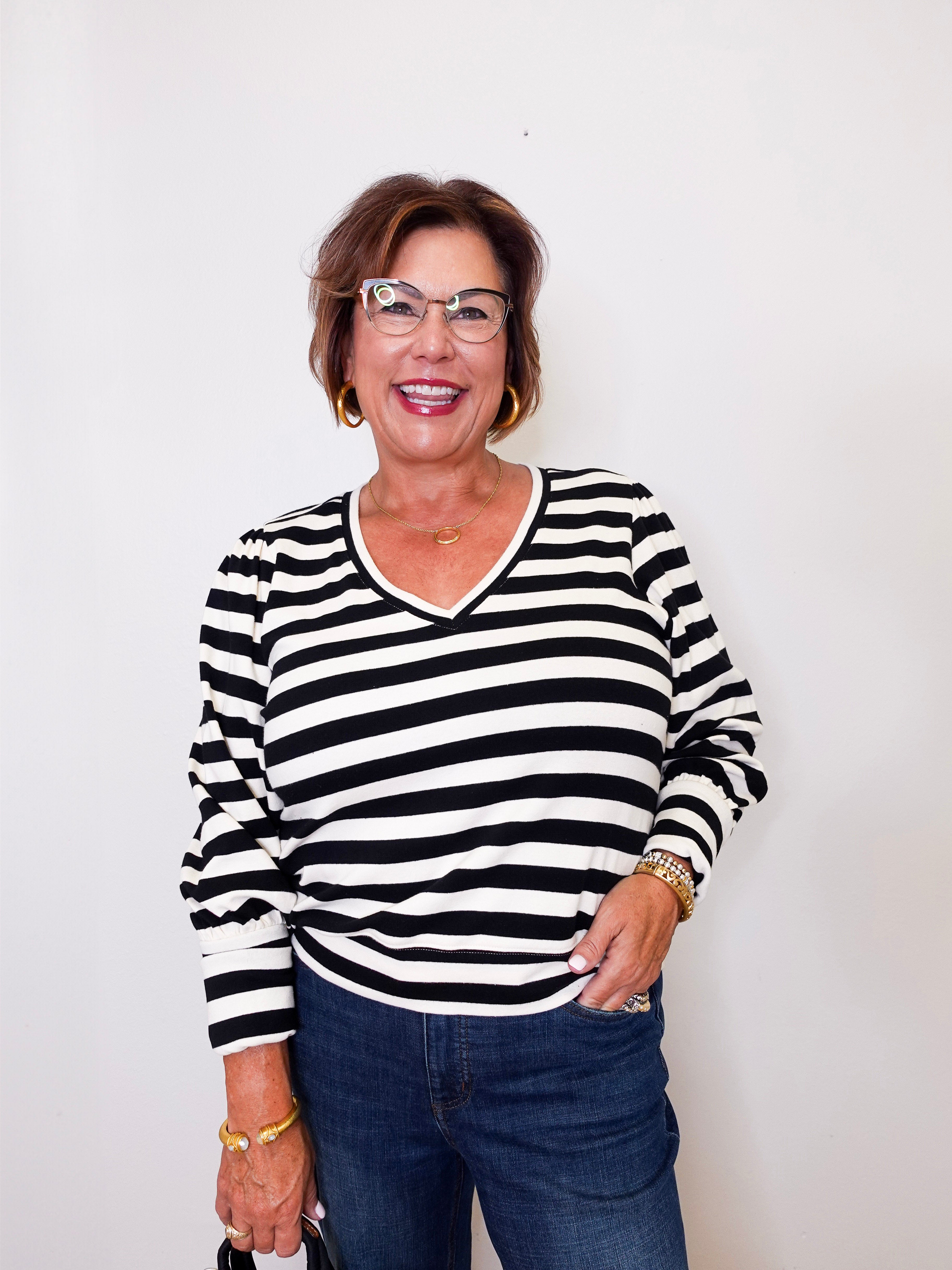 Woman wearing a black and white  Karen Kane striped shirt with blue jeans against a white background