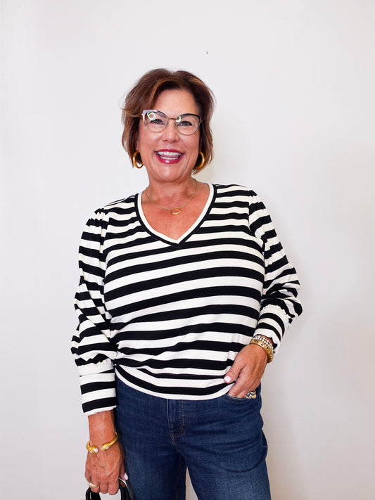 Woman wearing a black and white  Karen Kane striped shirt with blue jeans against a white background