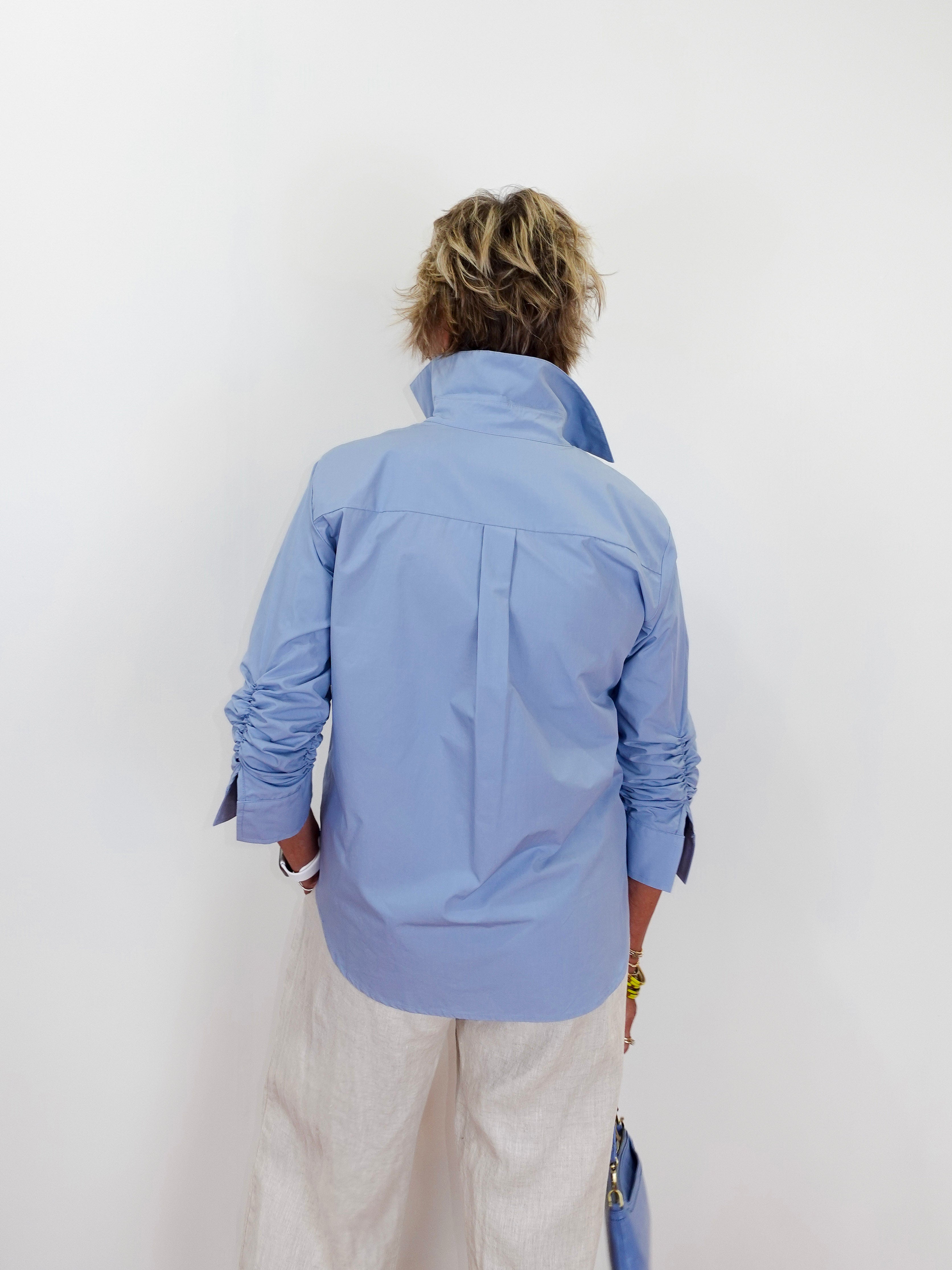 Person wearing a light blue jacket and beige pants against a white background