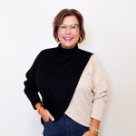 Woman wearing a black and beige sweater with blue jeans against a white background