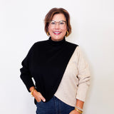 Woman wearing a black and beige sweater with blue jeans against a white background
