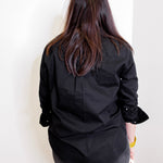 Person wearing a black top and pants against a white wall