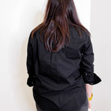 Person wearing a black top and pants against a white wall