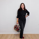 Woman in black shirt and jeans holding a colorful bag against a white wall.