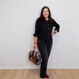 Woman in black shirt and jeans holding a colorful bag against a white wall.